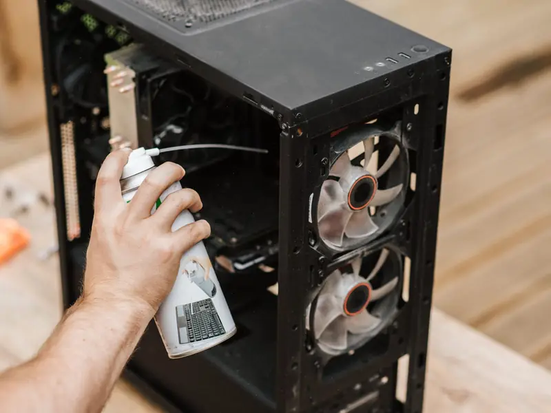 Foto ilustrativa: mão limpando um gabinete de computador aberto com ar comprimido