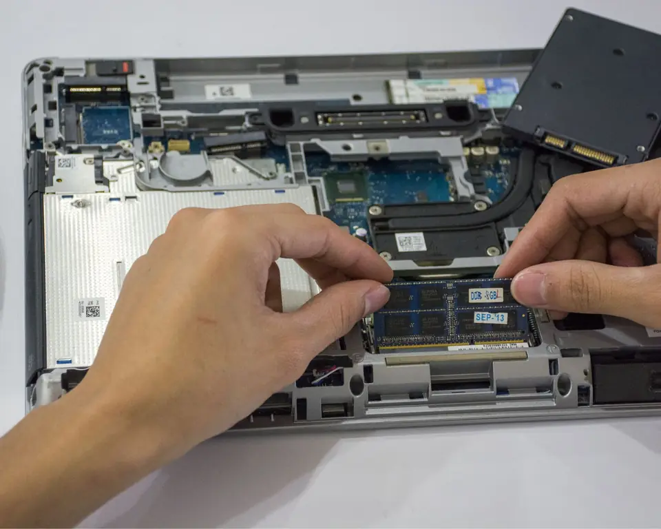 Foto ilustrativa: mãos de técnico encaixando um pente de memória num notebook aberto, com o SSD ao lado